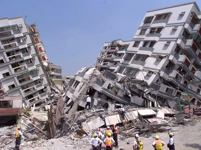 圖片顯示地震後倒塌的建築物,現場一片瓦礫。多名穿著制服的救援人員正在現場進行搜救工作,試圖尋找可能的倖存者。建築物結構嚴重損毀,場面令人震驚,突顯地震帶來的嚴重破壞。